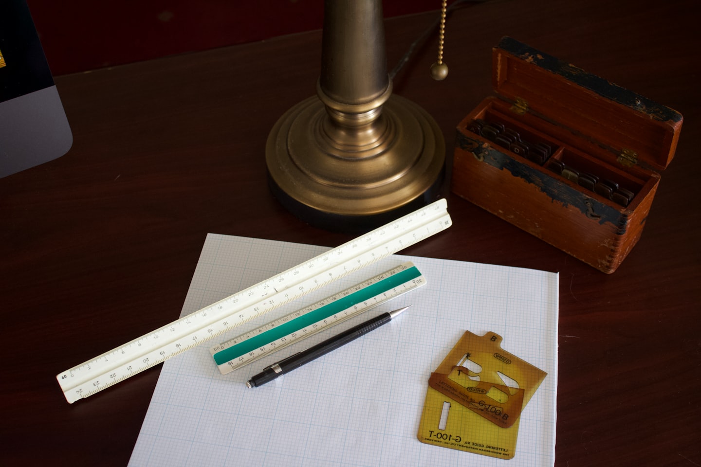 Drafting tools and graph paper on a dark wooden desk.