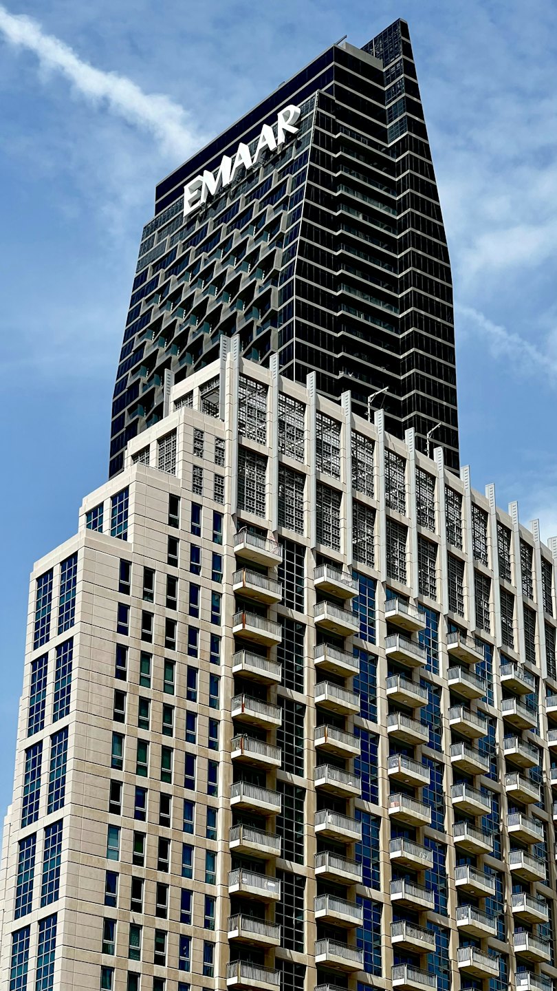 Two modern buildings with balconies reaching toward a blue sky.