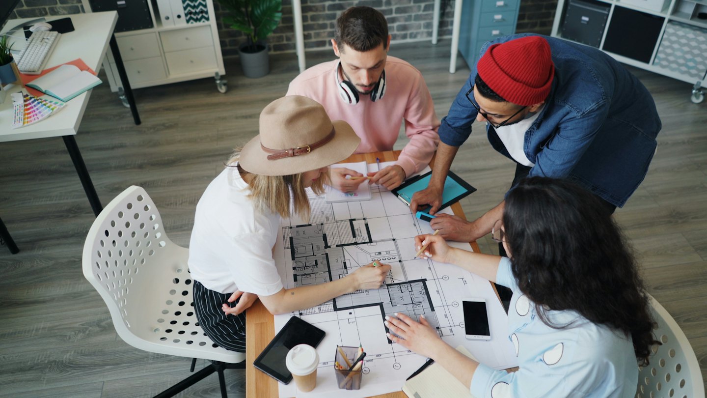 Four adults discussing blueprints on a wooden table.